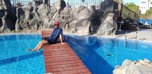 a man sitting on a ledge next to a swimming pool at Happy Fish Guest House in Patong Beach