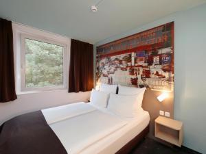 a bedroom with a white bed with a poster on the wall at B&B Hotel Berlin-Dreilinden in Kleinmachnow