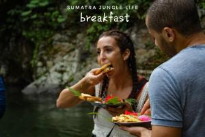 a woman eating a plate of food next to a man at Jungle life guesthouse Trekking & Transport Book with us in Bukit Lawang