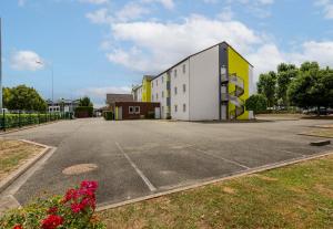 un aparcamiento vacío con un edificio blanco y amarillo en B&B HOTEL CHARTRES Le Coudray, en Chartres