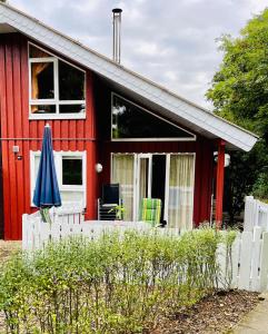 una casa roja con una valla blanca y una sombrilla en Extertal-Ferienpark - Premium Ferienhaus Sonnental - Sauna #50, en Extertal