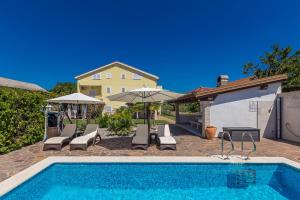 a swimming pool with chairs and umbrellas next to a house at Guest House Antonella in Malinska