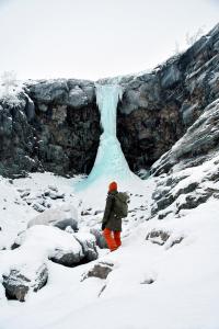 a person standing in the snow in front of a waterfall at Hostel Saana in Kilpisjärvi