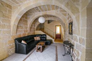 a living room with a black leather couch in a stone wall at 4 Bedroom Farmhouse with Large Private Pool in Xewkija