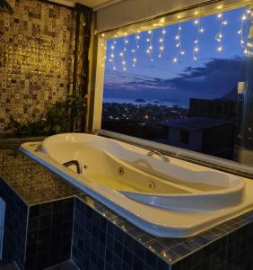 Suite Bela vista Muriqui Cantinho Feliz في مانغاراتيبا: حوض استحمام في الحمام مع نافذة مع أضواء