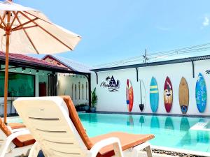 - une piscine avec des chaises et un parasol à côté d'un bâtiment avec des planches de surf dans l'établissement MeeJai Pool View Kohlarn, à Ko Larn