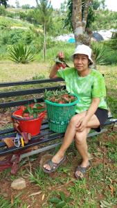 Eine Frau, die auf einer Bank mit einem Korb von Pflanzen sitzt. in der Unterkunft บ้านเพลินภู in Khao Kho