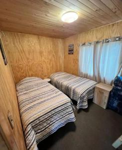 2 Betten in einem kleinen Zimmer mit Holzwänden in der Unterkunft Acogedora Casa de Campo Mocopulli in Dalcahue