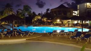 a swimming pool at night with chairs and tables at Le Cosy - Studio spacieux, équipé, proche Plage & Piscine, au Manganao in Saint-François