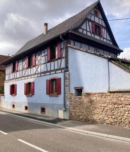 a white building with red shuttered windows on a street at Cocon à colombage alsacien "1789" in Innenheim