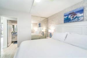 a white bedroom with a large bed and a mirror at Kanai a Nalu 314 - Newly Renovated, Oceanfront, AC in Wailuku