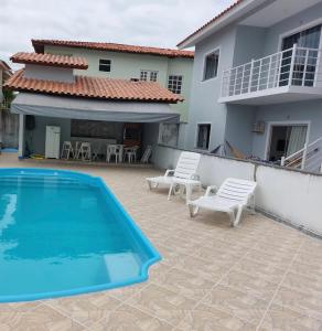 una piscina con 2 sillas blancas y una casa en apartamento vizinho ao mar, en Porto Seguro