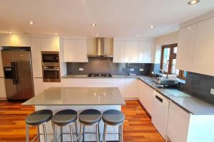 una cocina con una isla con 4 taburetes en Luxury London House Sleeps x 16, Free Parking, Free Wifi, Garden Patio, Close to tube line easy access to Central London, en Ilford