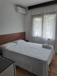 a bedroom with a large bed with white sheets and a window at Vitória Torres Hotel in Torres