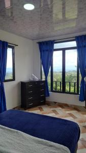 1 dormitorio con cortinas azules, 1 cama y ventana en Hospedaje Villa Salome, en Pereira