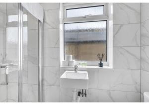 La salle de bains blanche est pourvue d'un lavabo et d'une fenêtre. dans l'établissement A Place to Dream: Airy Studio in Serene Locale, à Londres