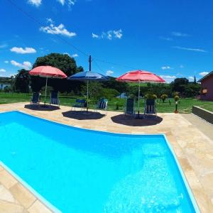 a swimming pool with two umbrellas and chairs and tables at Eco Pousada Sinhá Ruth - Aventura & Descanso in Brotas