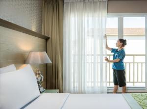 una mujer abriendo una ventana en una habitación de hotel en Best Western Patong Beach, en Patong Beach