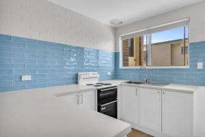 a kitchen with white cabinets and blue tiles at Marine Court - Unit 6 in Merimbula