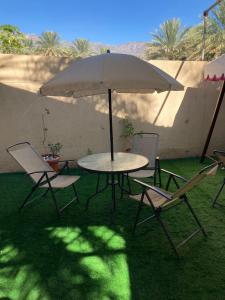 a table and chairs with an umbrella in the grass at Reef Alhamra in Al Ḩamrāʼ