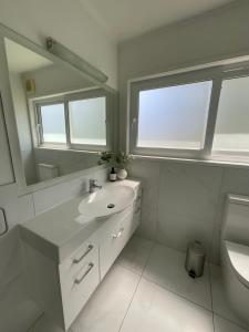 a white bathroom with a sink and a mirror at Central Howick Uxbridge Apartments in Auckland