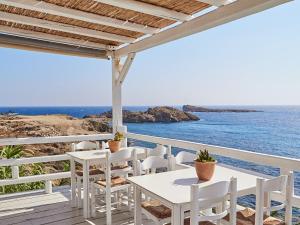 a patio with white tables and chairs and the ocean at Mykonos Lolita, A Grecotel Resort to Live in Agios Sostis Mykonos