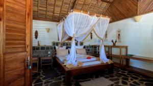 a bedroom with a canopy bed with white curtains at Ravoravo Beachfront Family lodge in Lokobe National Park-Nosy be, autentic Madagascar expiriance with europian confort in Antafondro