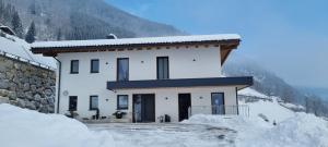 Una casa blanca con nieve al costado. en Apartment Talblick, en Bramberg am Wildkogel