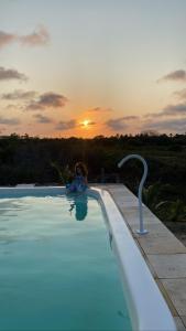 una persona sentada en una piscina con la puesta de sol en Villasollagoinha, en Paraipaba