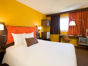 パンタンにあるメルキュール パリ ポルト デ パンタンの大きな白いベッドと黄色の壁が備わるホテルルームです。
