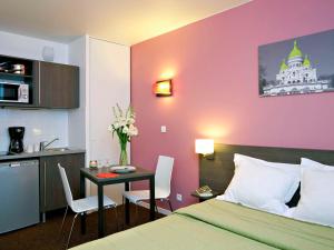 Cet appartement comprend une chambre avec un lit et une table ainsi qu'une cuisine. dans l'établissement Aparthotel Adagio Access Paris Asnières, à Asnières-sur-Seine