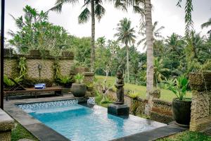 a pool in the middle of a garden with palm trees at Alvia Joglo House & Private Pool in Tampaksiring