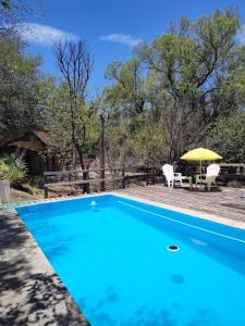 a blue swimming pool with a table and umbrella at Cabañas Budapest in Capilla del Monte