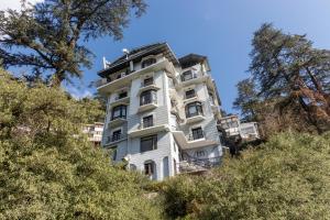 a white building on a hill with trees at Treebo The Alpine Heritage Residency in Shimla