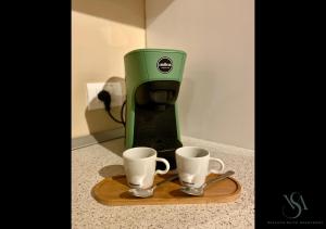 eine grüne Kaffeemaschine mit zwei Tassen auf einem Schneidebrett in der Unterkunft Velluto Suite Apartment in Calderara di Reno