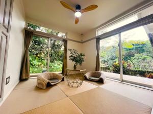 a living room with a ceiling fan and large windows at Yama'oto - Nature Luxury Stay in Motobu