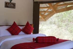 sypialnia z łóżkiem z czerwonymi poduszkami i oknem w obiekcie Mara Empiris Safari Camp w mieście Ololaimutiek