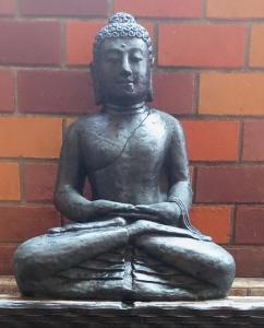 une statue d'une personne assise devant un mur de briques dans l'établissement ZEN MOON Hostel, à Yogyakarta