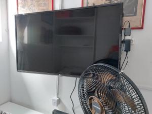 a flat screen tv hanging on a wall with a fan at PEQUENO QUARTO individual-PERTO DO CENTRO DE CONVENÇÕES- RECIFE - ventilador,TV,mesa de trabalho in Recife
