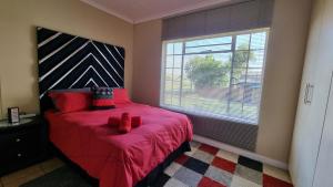 Schlafzimmer mit einem Bett mit roten Kissen und einem Fenster in der Unterkunft Sunrise Serenity Guest House in Lydenburg