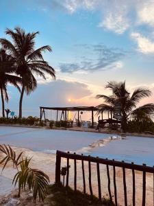 een bankje op een strand met palmbomen en de zonsondergang bij Hotel Arenas Mahahual in Mahahual