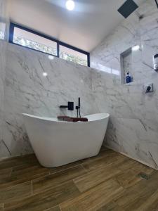 y baño con bañera blanca y paredes de mármol. en Villa El Bosque Dorado en Fortuna