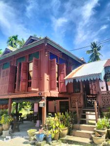 a wooden house with red shuttered windows and plants at Homestay Teratak Kayu kota Aur in Kepala Batas