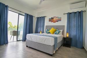 1 dormitorio con 1 cama con cortinas azules y ventana en Sunset Haven Villa en Beau Vallon