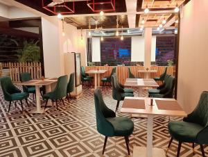 Skon Baga Bliss Hotel by Orion Hotels في Goa: مطعم بطاولات خشبية وكراسي خضراء