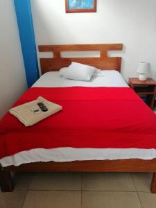 Una cama con una manta roja y un mando a distancia. en Descanso del Petrel en Puerto Ayora