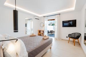 Oliving Mykonos Luxury Suites في Klouvas: غرفة نوم بيضاء مع سرير وتلفزيون