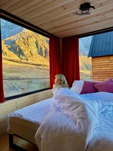 a woman laying in bed looking out of a window at Kazbegi Inn Cottages in Stepantsminda