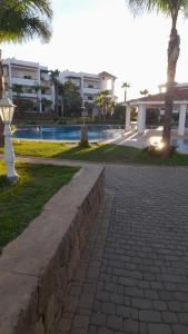 einen Backsteinsteg neben einem Gebäude und einem Pool in der Unterkunft Marina Golf appartement de luxe in Asilah