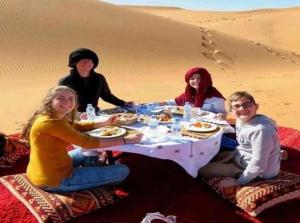 Merzouga Top Luxury Camp في مرزوقة: مجموعة من الناس يجلسون حول طاولة في الصحراء